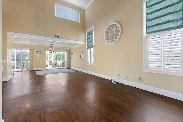 unfurnished living room featuring a high ceiling, ornamental molding, dark hardwood / wood-style floors, and a chandelier