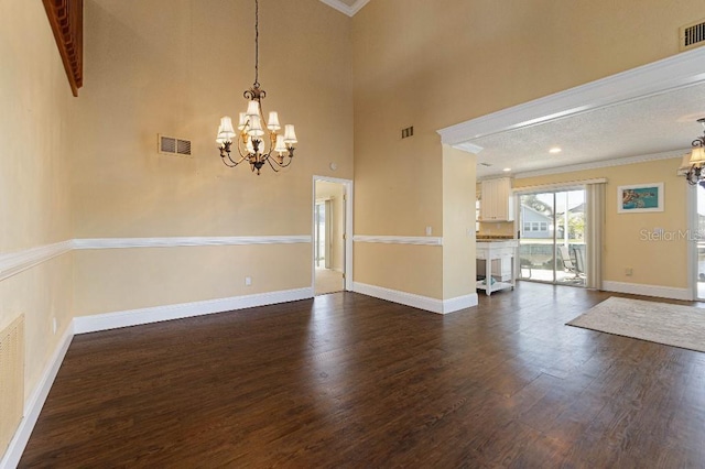 empty room featuring dark hardwood / wood-style flooring, crown molding, a chandelier, and a high ceiling