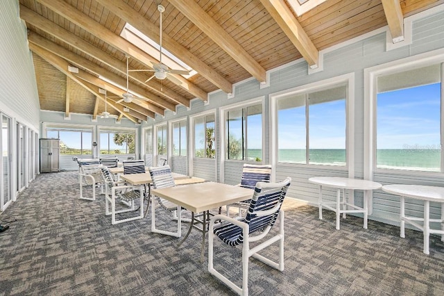 sunroom / solarium with plenty of natural light, vaulted ceiling with skylight, a beach view, and a water view