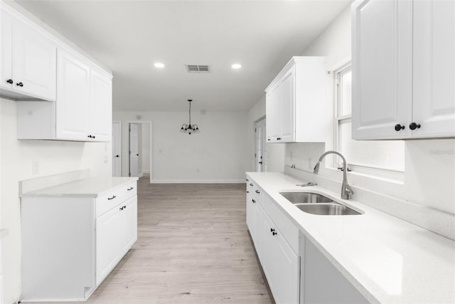 kitchen with light hardwood / wood-style floors, sink, white cabinetry, and pendant lighting