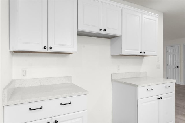 kitchen featuring white cabinetry, light stone countertops, and wood-type flooring