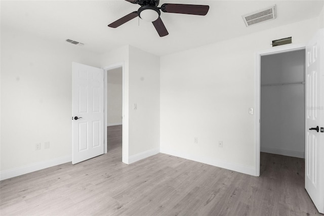 unfurnished bedroom with light hardwood / wood-style flooring, a closet, ceiling fan, and a walk in closet