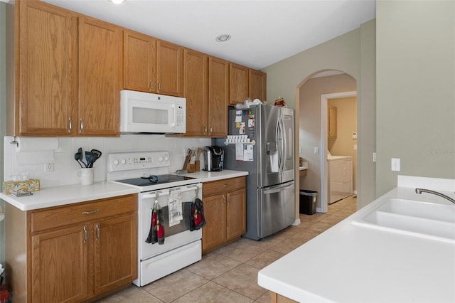 kitchen with washer / dryer, sink, light tile patterned floors, white appliances, and decorative backsplash