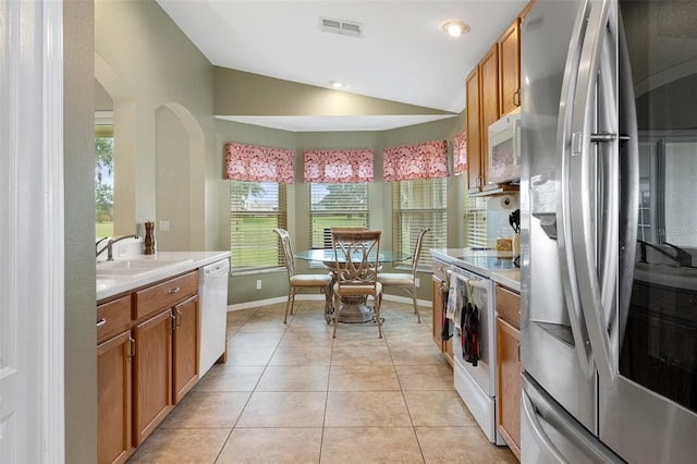 kitchen with sink, white appliances, vaulted ceiling, and light tile patterned floors