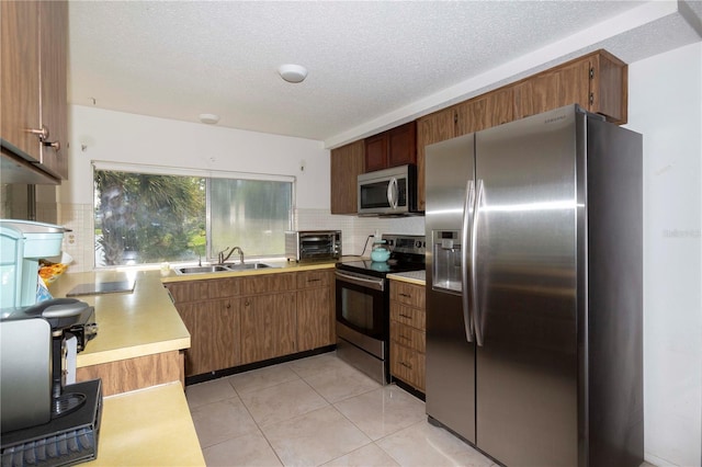 kitchen with a textured ceiling, appliances with stainless steel finishes, backsplash, light tile patterned floors, and sink