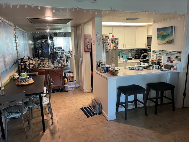 kitchen with decorative backsplash, kitchen peninsula, white cabinets, stainless steel fridge, and light tile patterned floors