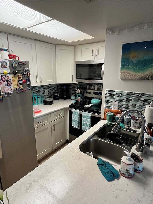 kitchen featuring decorative backsplash, light stone counters, white cabinets, stainless steel appliances, and sink