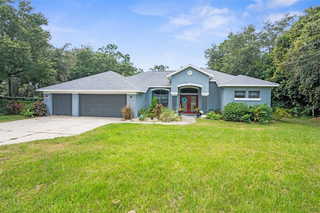 ranch-style house with driveway, an attached garage, french doors, a front lawn, and stucco siding