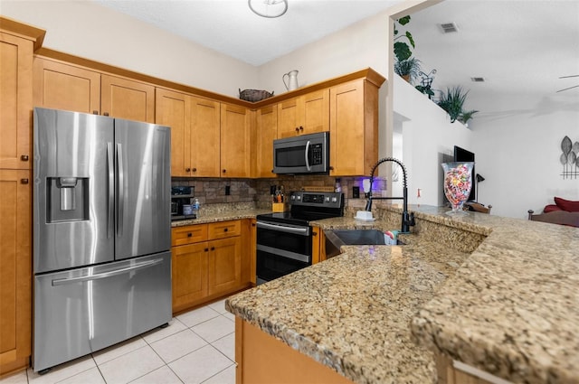 kitchen with light stone counters, appliances with stainless steel finishes, light tile patterned floors, tasteful backsplash, and sink