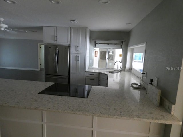 kitchen with ceiling fan, light stone counters, black electric cooktop, sink, and stainless steel fridge