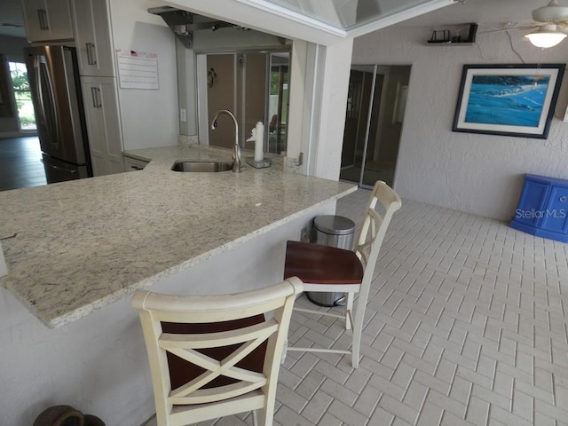 kitchen featuring sink, stainless steel refrigerator, kitchen peninsula, and light stone countertops