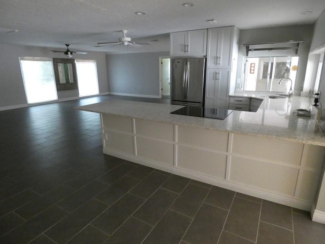 kitchen featuring ceiling fan, black electric stovetop, stainless steel refrigerator, light stone counters, and sink