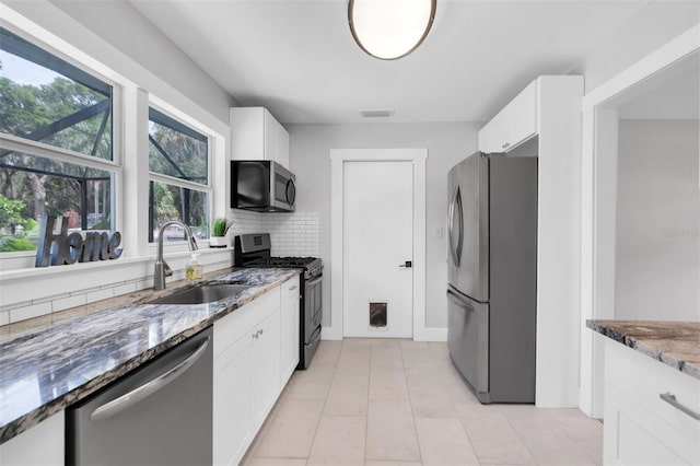 kitchen featuring sink, appliances with stainless steel finishes, tasteful backsplash, white cabinets, and dark stone counters