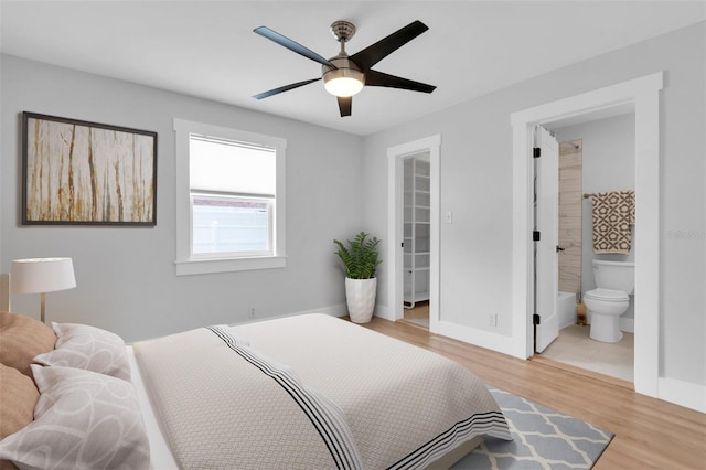 bedroom with ensuite bathroom, a spacious closet, light hardwood / wood-style flooring, a closet, and ceiling fan