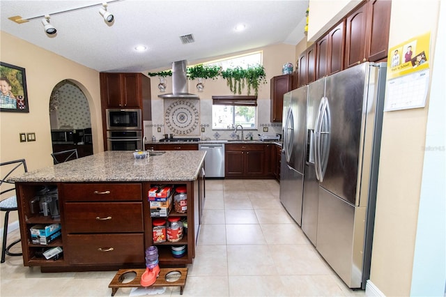 kitchen with light stone counters, wall chimney range hood, light tile patterned floors, a center island, and stainless steel appliances