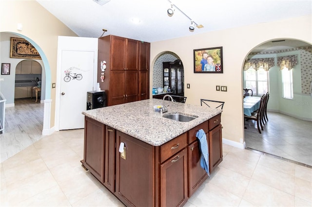 kitchen with an island with sink, light stone countertops, track lighting, light tile patterned floors, and sink