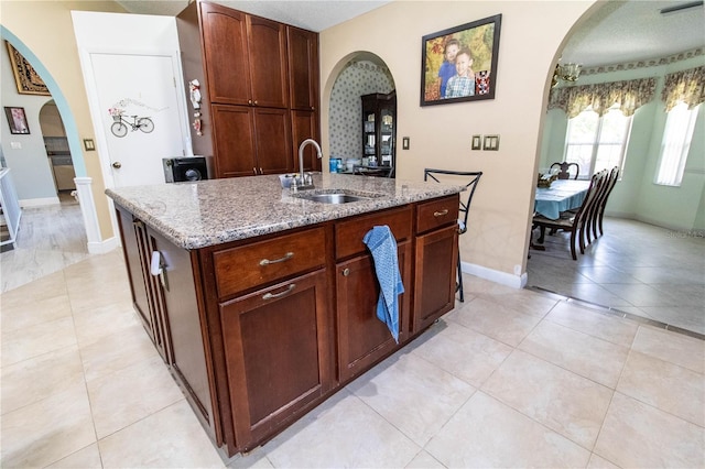 kitchen featuring sink, light stone counters, light tile patterned floors, and a kitchen island with sink