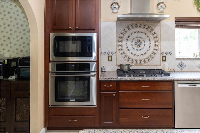 kitchen featuring wall chimney range hood, stainless steel appliances, and backsplash