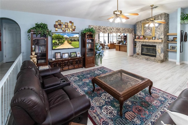 living room featuring light wood-type flooring, a fireplace, a textured ceiling, lofted ceiling, and ceiling fan