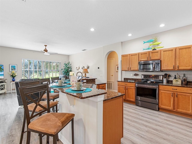 kitchen featuring a kitchen island with sink, sink, a kitchen breakfast bar, appliances with stainless steel finishes, and ceiling fan