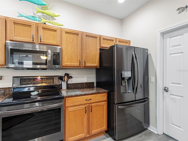 kitchen with dark stone countertops, light hardwood / wood-style floors, and appliances with stainless steel finishes