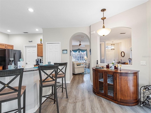 kitchen with stainless steel fridge with ice dispenser, kitchen peninsula, a kitchen bar, hanging light fixtures, and light hardwood / wood-style flooring