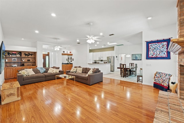 living room featuring light wood-style floors, recessed lighting, a brick fireplace, and ceiling fan