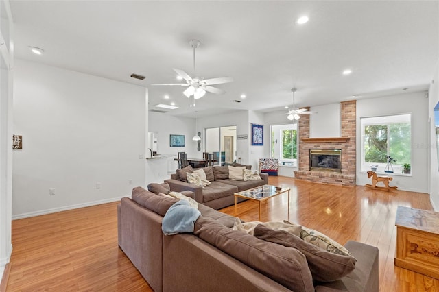 living area featuring recessed lighting, a brick fireplace, a healthy amount of sunlight, and light wood finished floors