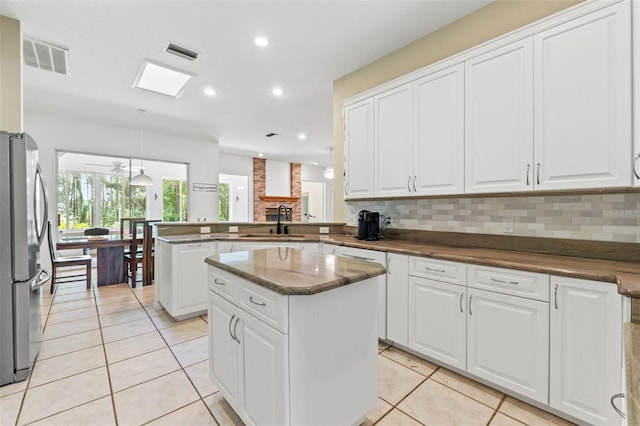 kitchen featuring tasteful backsplash, visible vents, freestanding refrigerator, a peninsula, and a sink