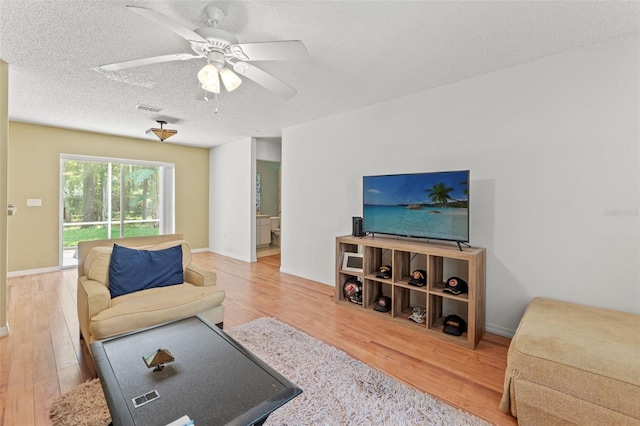 living room with a textured ceiling, wood finished floors, visible vents, baseboards, and a ceiling fan