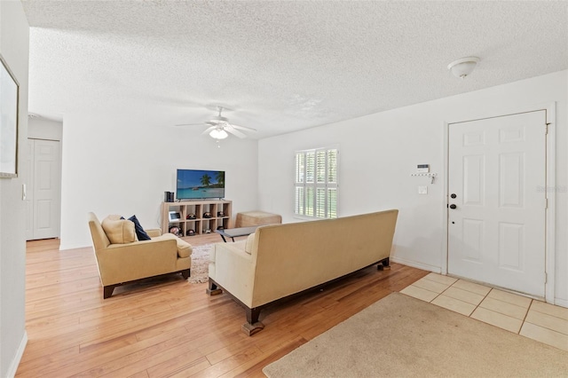 living room with light wood-style flooring, ceiling fan, and a textured ceiling