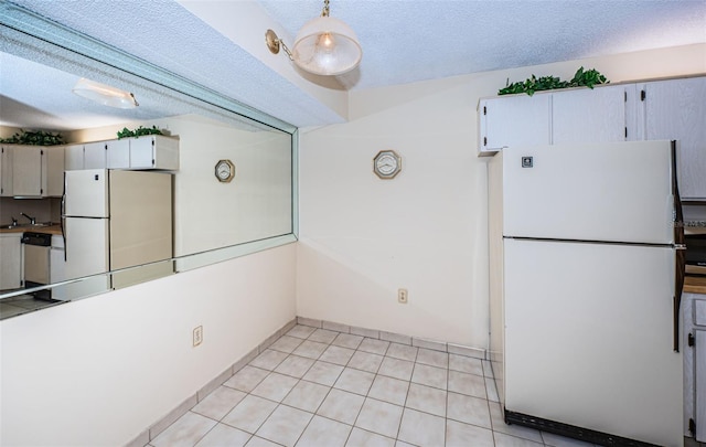 kitchen with light tile patterned floors, sink, a textured ceiling, and white refrigerator