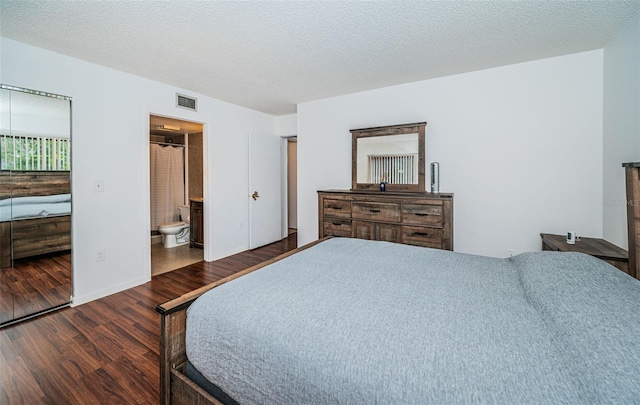 bedroom with a textured ceiling, dark hardwood / wood-style floors, and connected bathroom