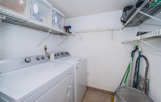 clothes washing area featuring light tile patterned flooring, washer and clothes dryer, and a textured ceiling