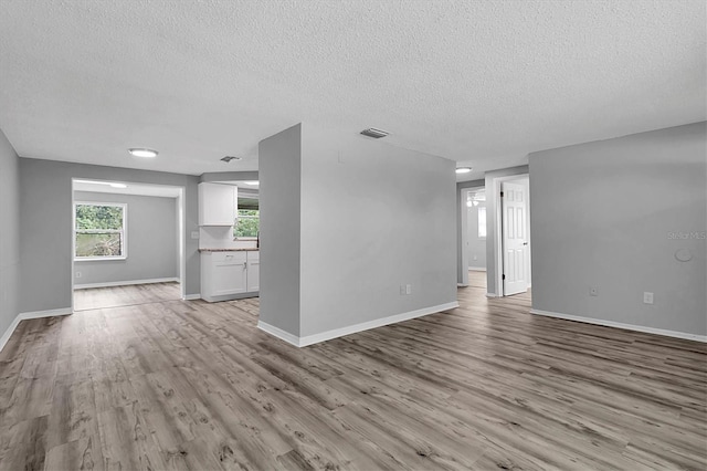 unfurnished living room with visible vents, a textured ceiling, light wood-style flooring, and baseboards