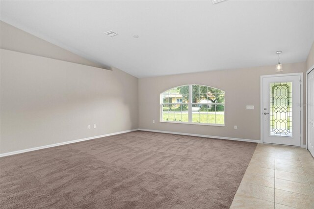 unfurnished living room with lofted ceiling, light tile patterned floors, light colored carpet, visible vents, and baseboards