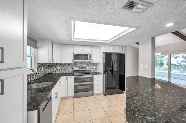 kitchen with appliances with stainless steel finishes, light tile patterned flooring, white cabinetry, and dark stone counters