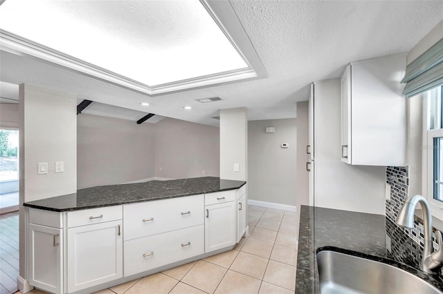 kitchen featuring light tile patterned floors, a textured ceiling, a sink, and white cabinetry