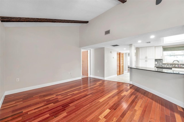 unfurnished living room with beam ceiling, high vaulted ceiling, light tile patterned floors, and sink