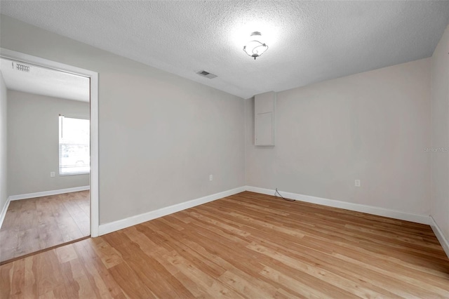 unfurnished room featuring light wood-type flooring, baseboards, visible vents, and a textured ceiling