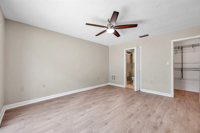 unfurnished bedroom featuring light wood-style floors, baseboards, visible vents, and a walk in closet