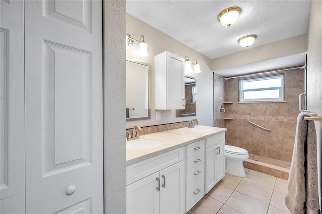 bathroom with double vanity, tiled shower, a sink, and toilet