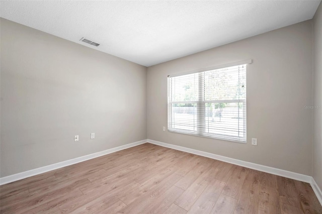 empty room with a textured ceiling, light wood finished floors, visible vents, and baseboards