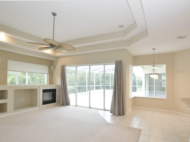 unfurnished living room featuring a raised ceiling, light tile patterned flooring, and ceiling fan