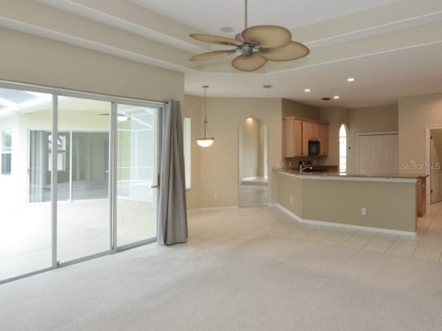 unfurnished living room featuring ceiling fan, a raised ceiling, and light carpet