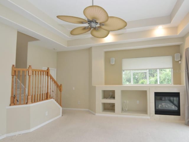 unfurnished living room with ceiling fan, a tray ceiling, carpet floors, and built in features