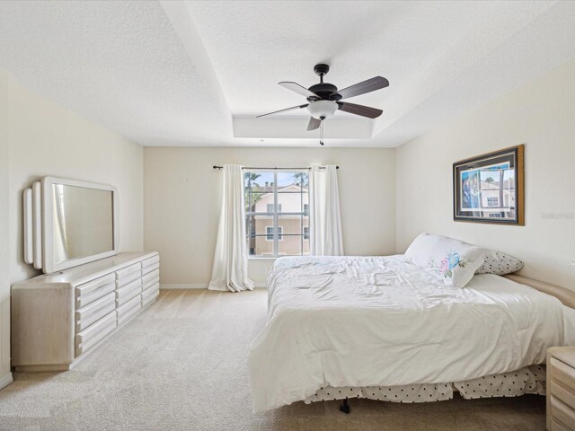 bedroom with a tray ceiling, ceiling fan, light carpet, and a textured ceiling