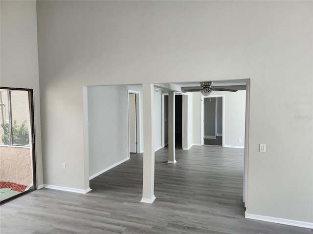 empty room featuring a towering ceiling, a ceiling fan, baseboards, and wood finished floors