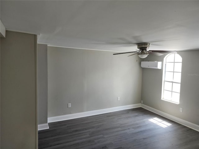 spare room featuring dark wood-type flooring, a wall unit AC, baseboards, and a ceiling fan