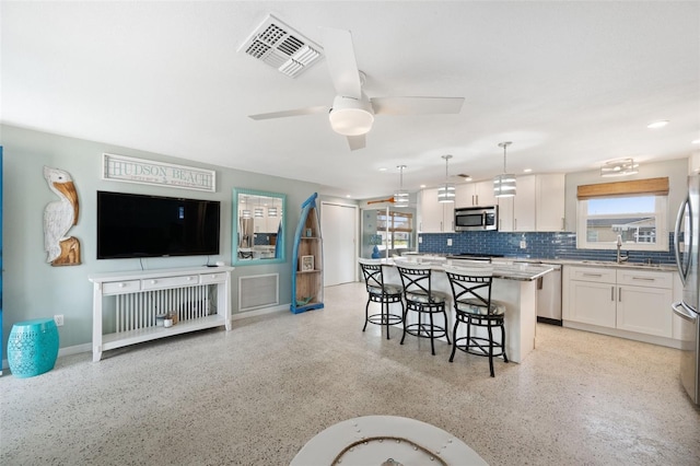 interior space with appliances with stainless steel finishes, white cabinetry, pendant lighting, a kitchen island, and ceiling fan